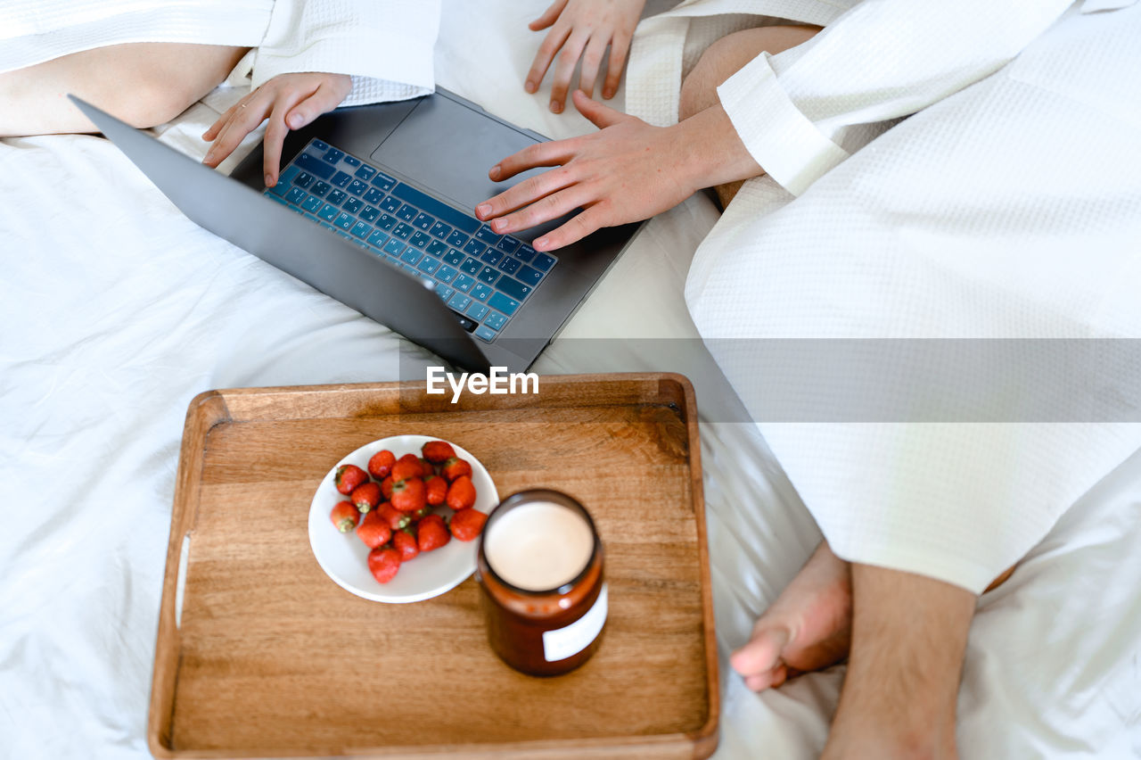 Young couple watching movie on laptop. they are in bed in white bathrobes. breakfast, strawberries
