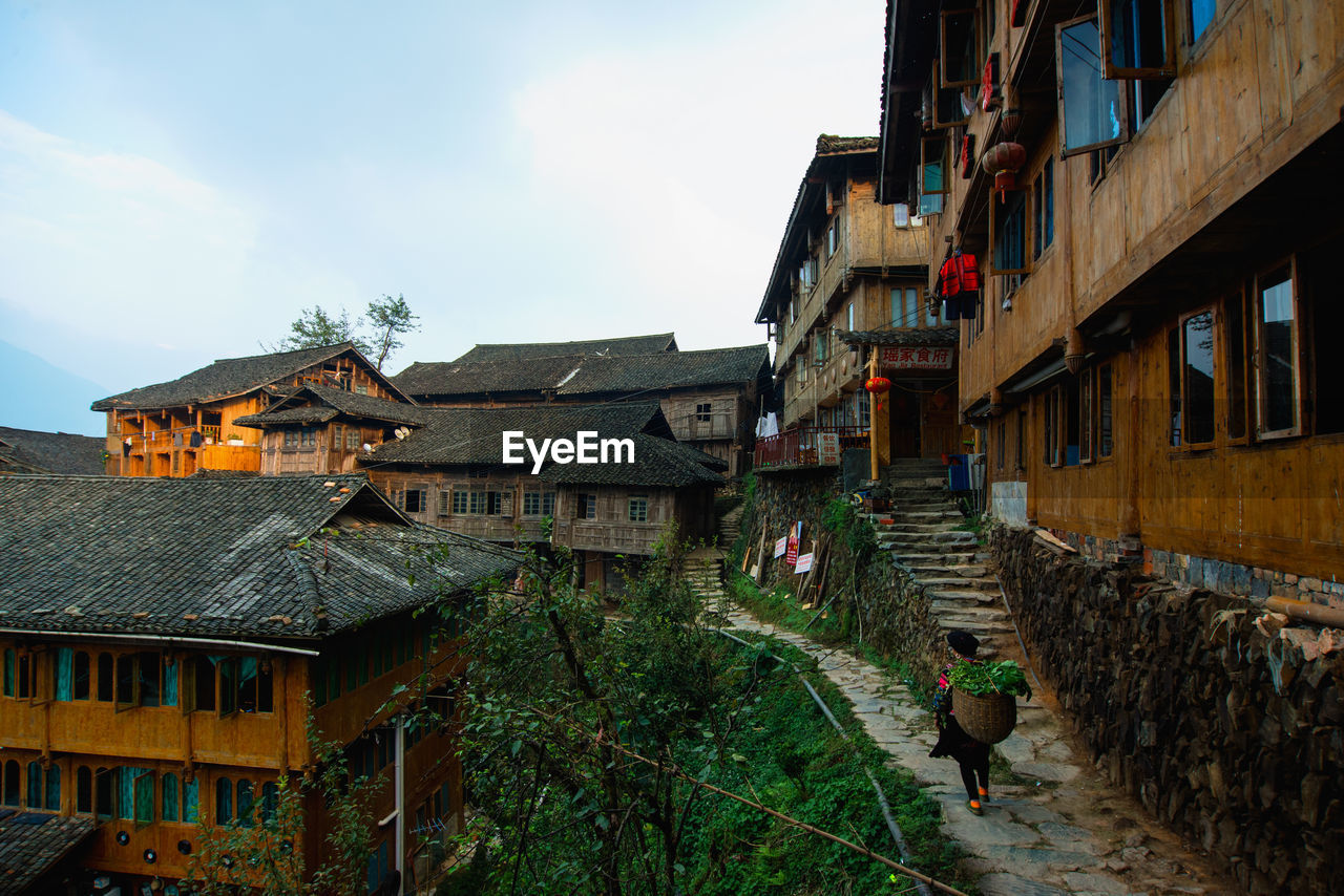 Rear view of woman with wicker basket while walking amidst houses