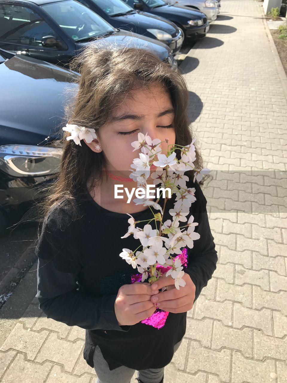 Girl smelling white flowers on walkway during sunny day