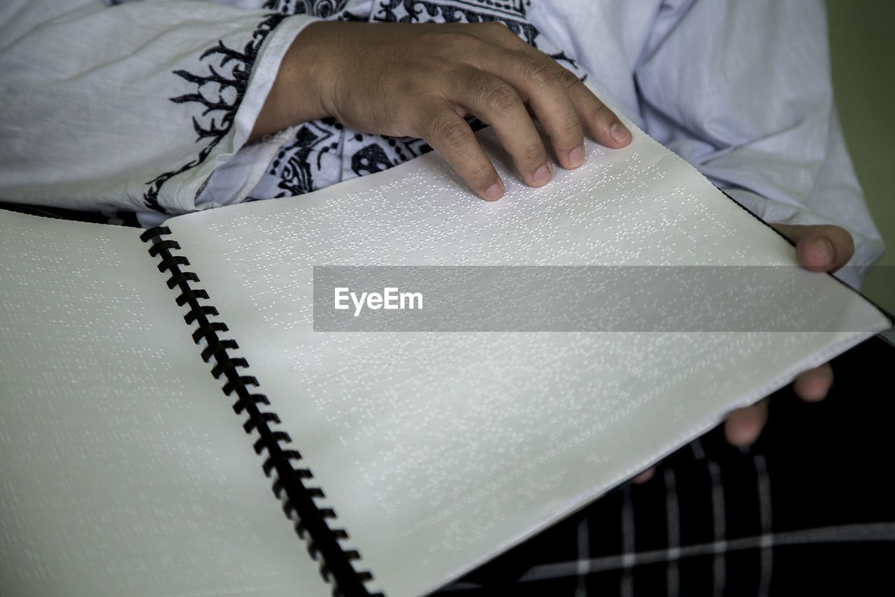 Midsection of blind person reading bible in braille