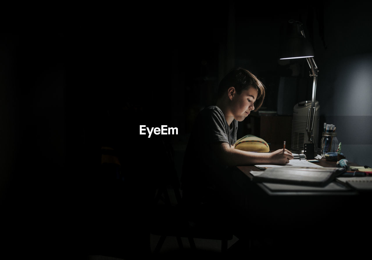 Side view of boy studying at table in darkroom
