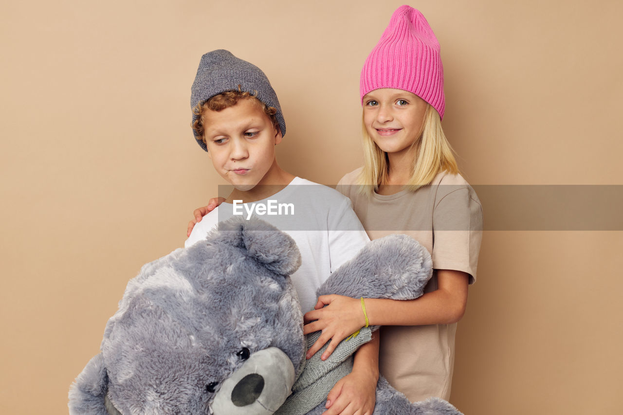 Sibling with stuffed toy against beige background