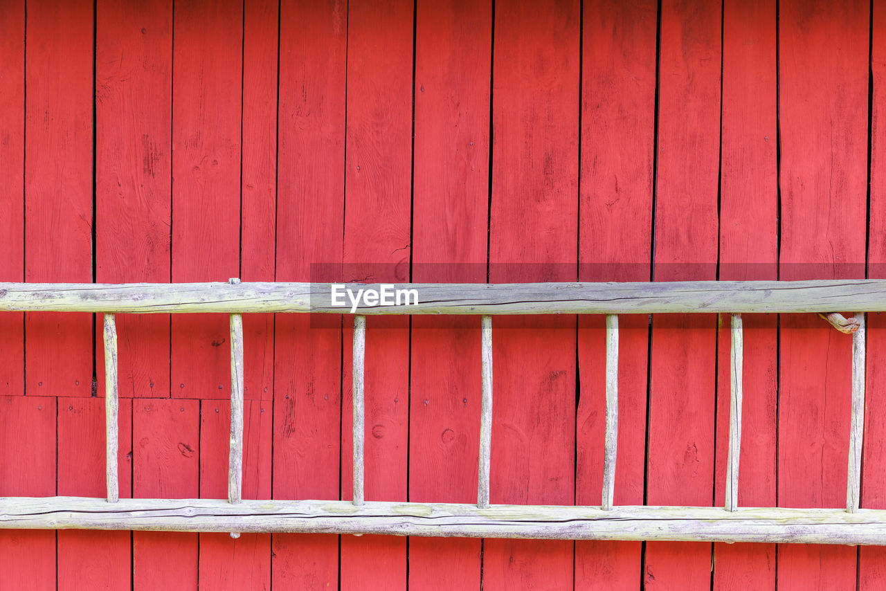 Old wooden ladder on a red wooden wall