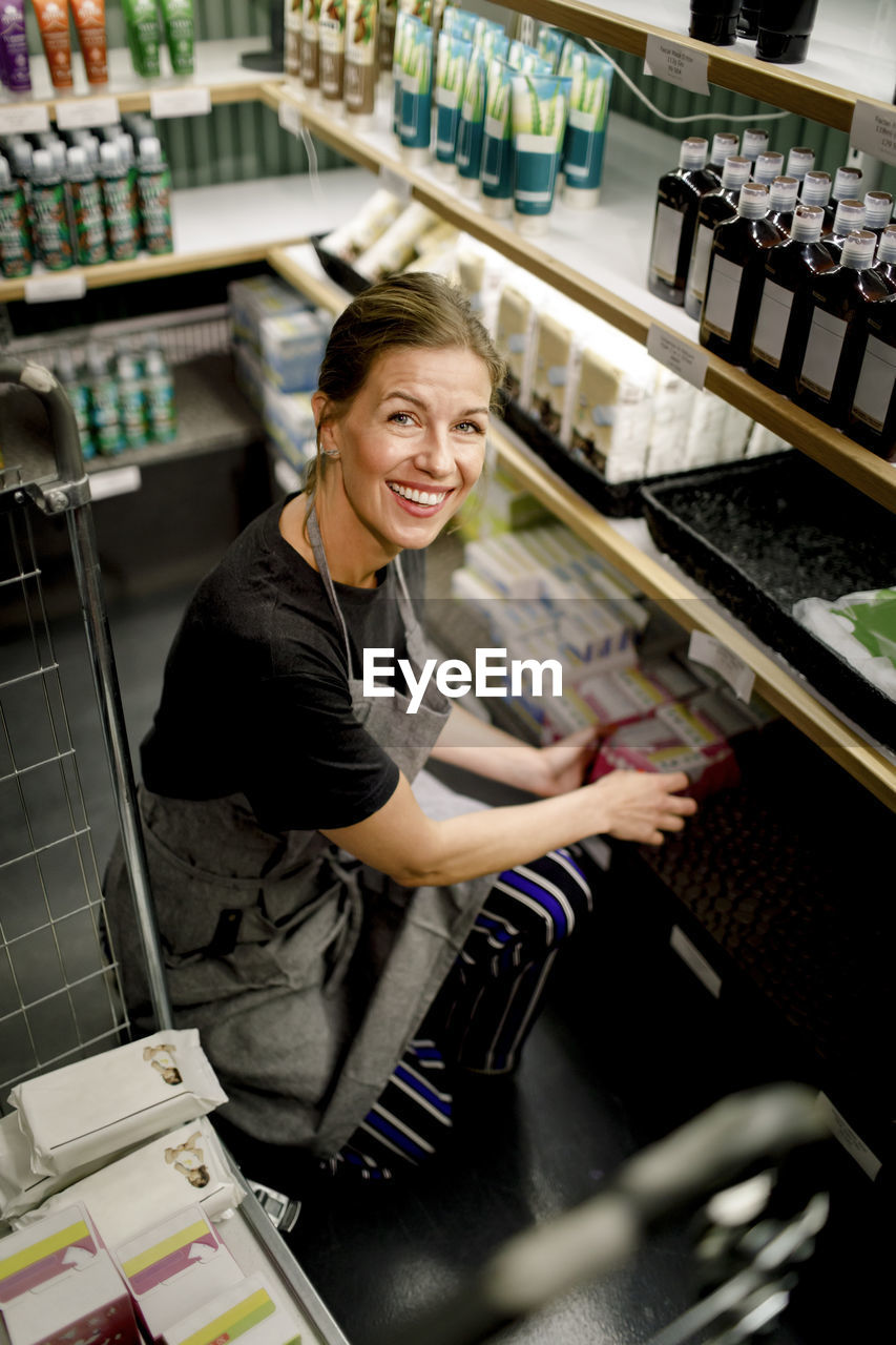 Portrait of smiling saleswoman crouching while working in supermarket