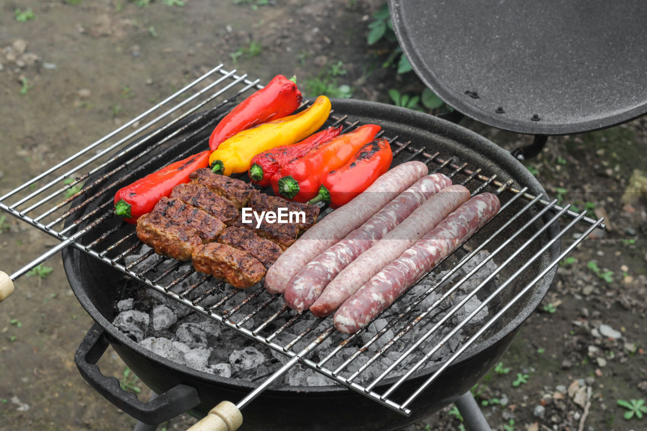 Raw sausages, cutlets and peppers on the grill grate.