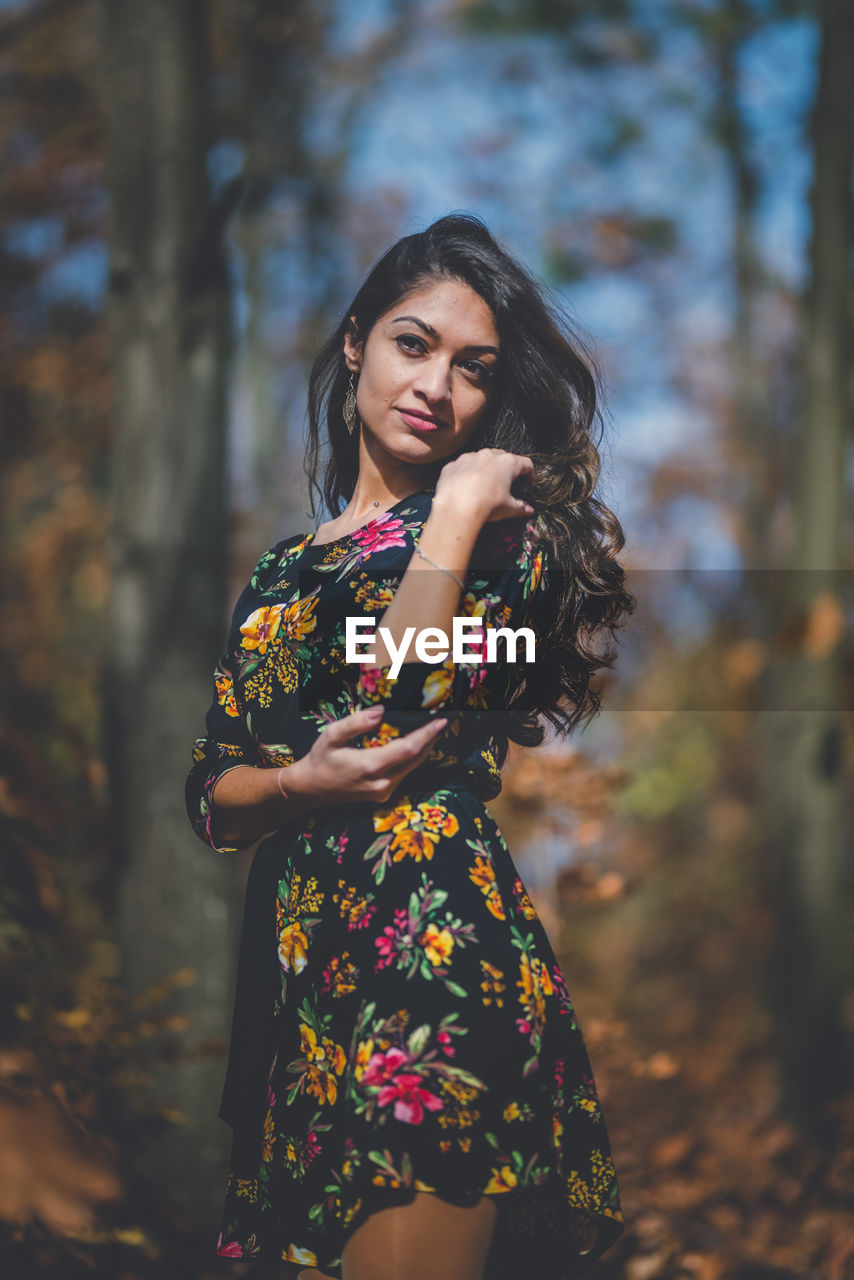 Young woman looking away while standing against tree