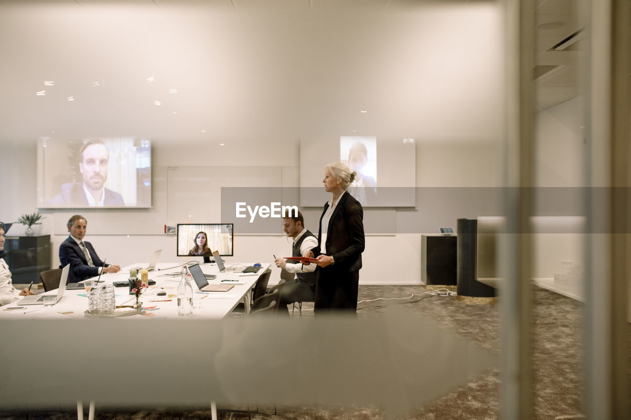 Mature businesswoman giving presentation in board room during global conference meeting at office