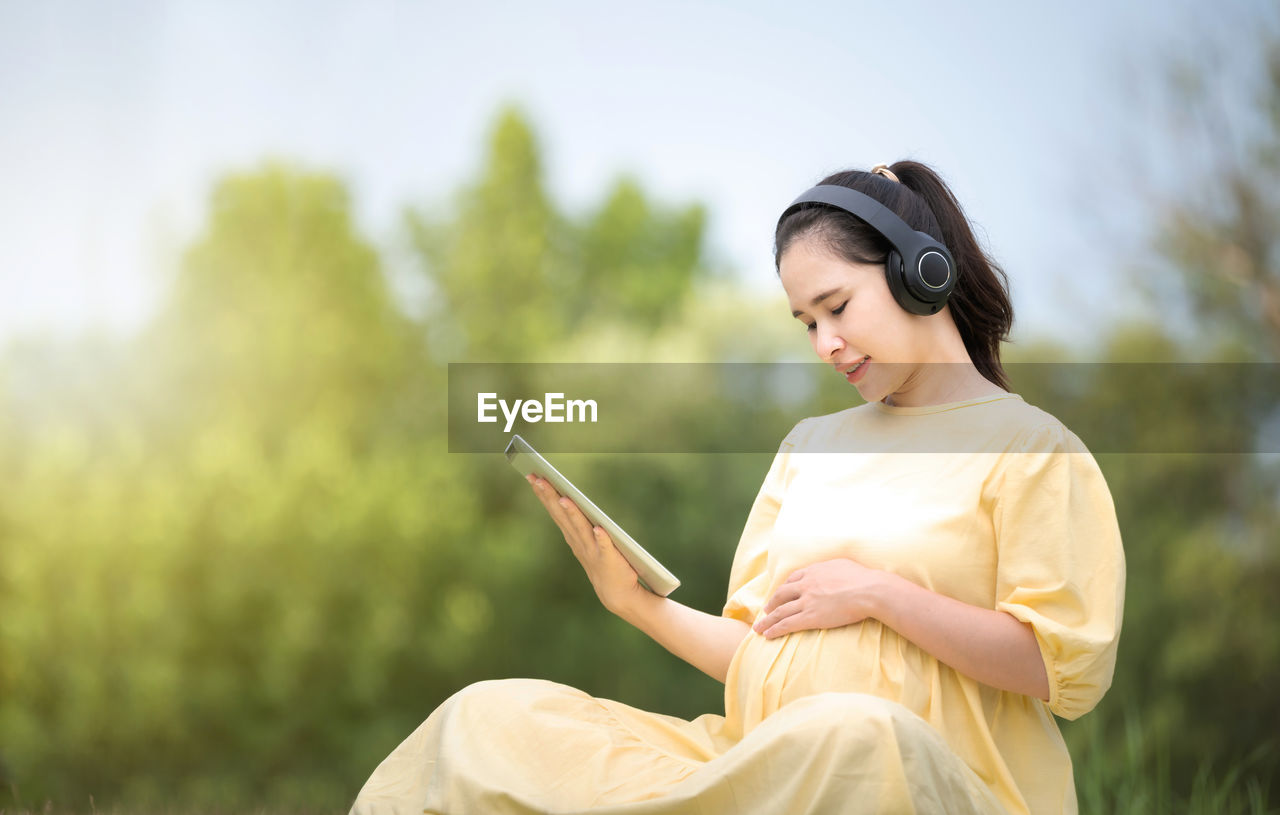 SIDE VIEW OF YOUNG WOMAN USING SMART PHONE OUTDOORS