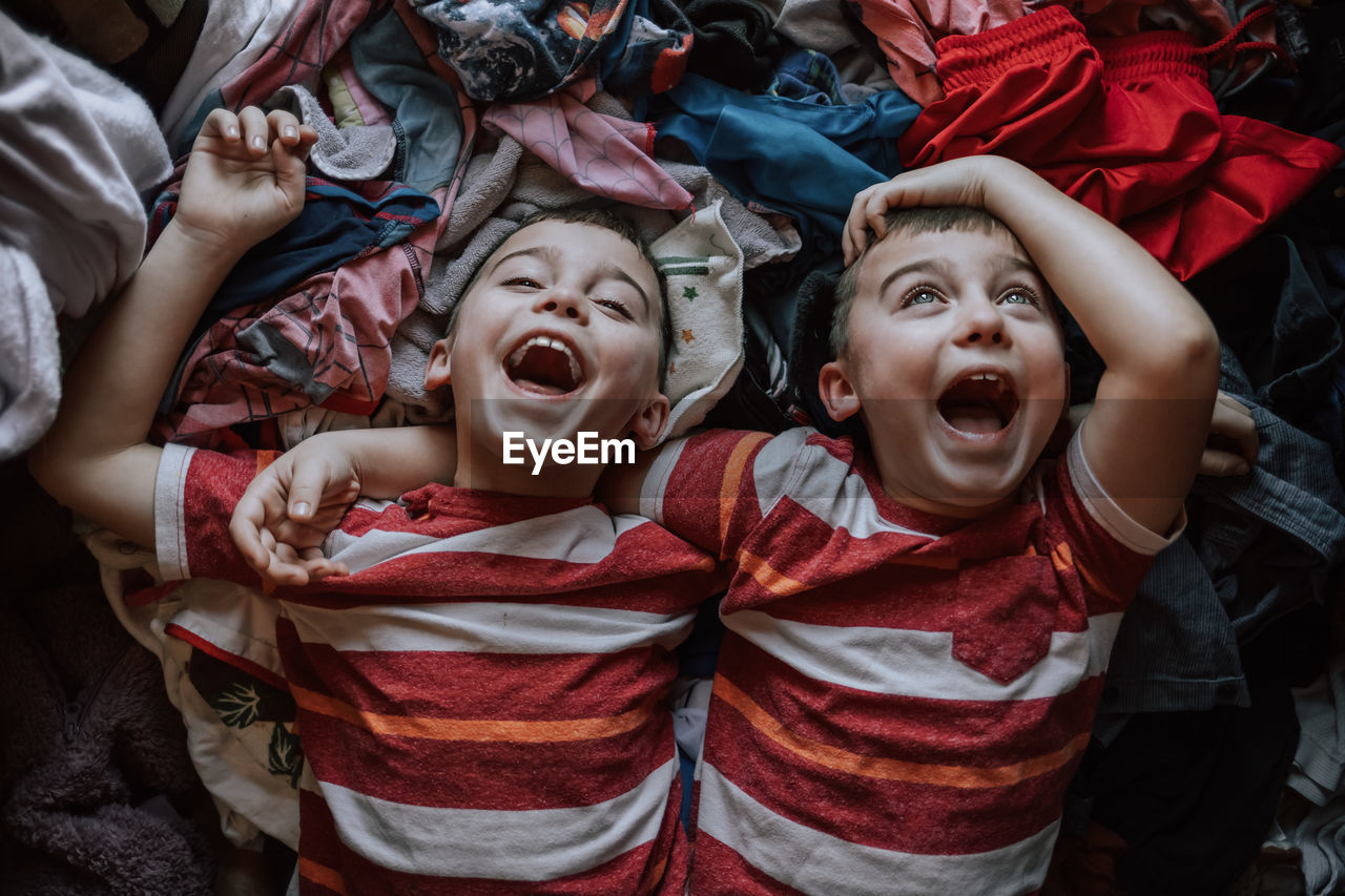 High angle view of laughing boys lying on clothes at home