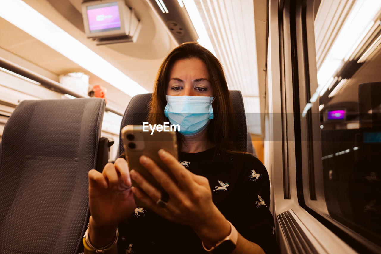 PORTRAIT OF YOUNG WOMAN USING MOBILE PHONE WHILE SITTING IN BUS