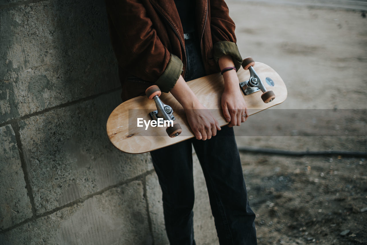 Midsection of woman holding skateboard while standing against wall