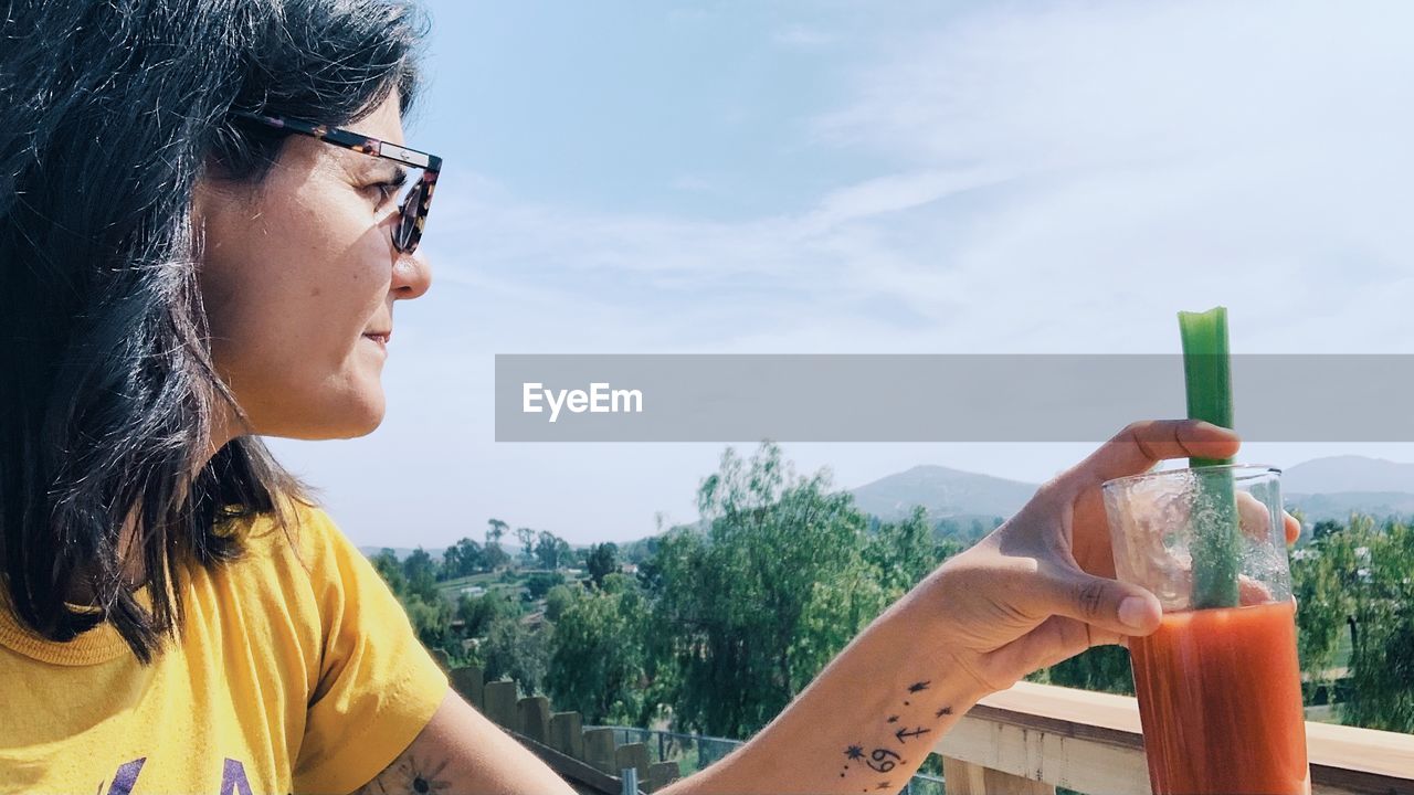 PORTRAIT OF WOMAN HOLDING CAMERA AGAINST SKY