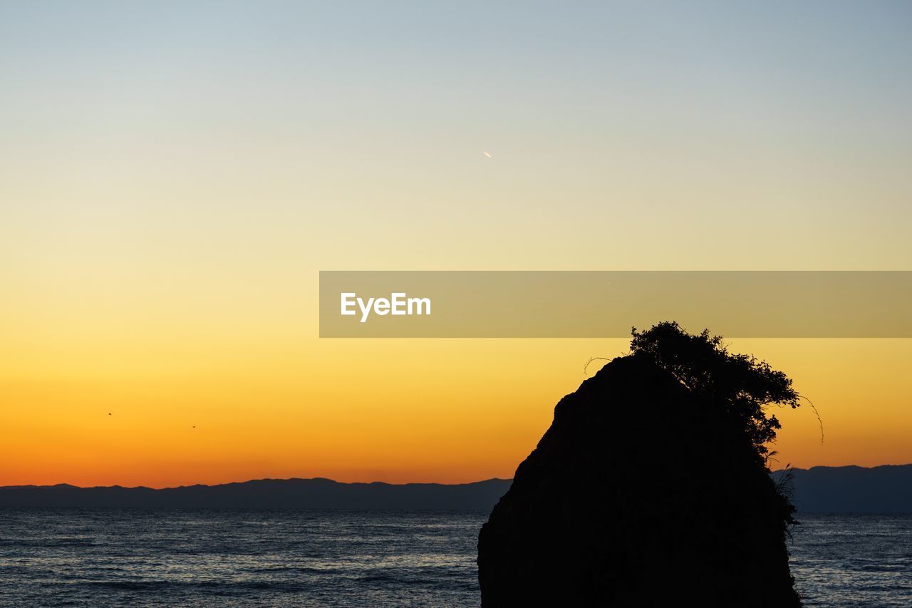 Silhouette of cliff at seashore during sunset