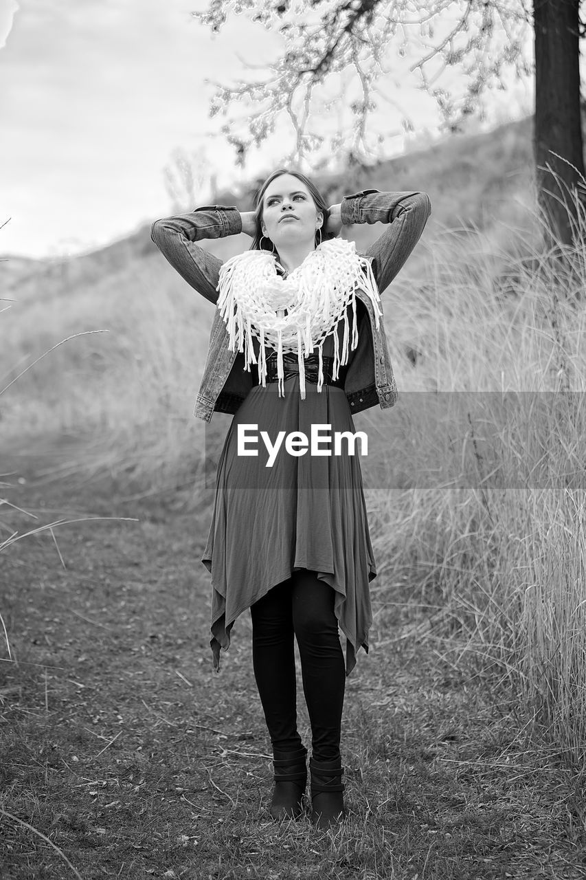 Young woman with hands behind head standing on footpath