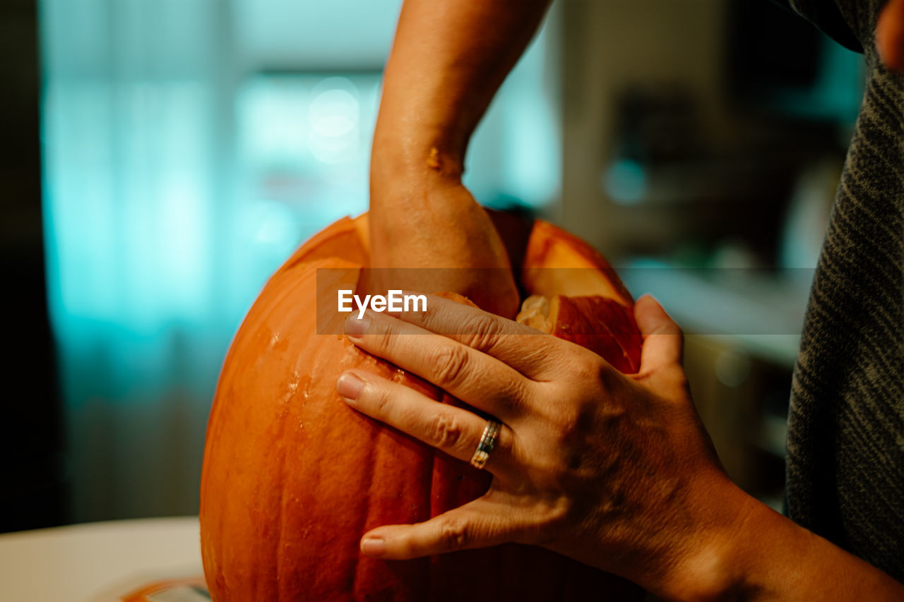 Midsection of person carving pumpkin on table at home