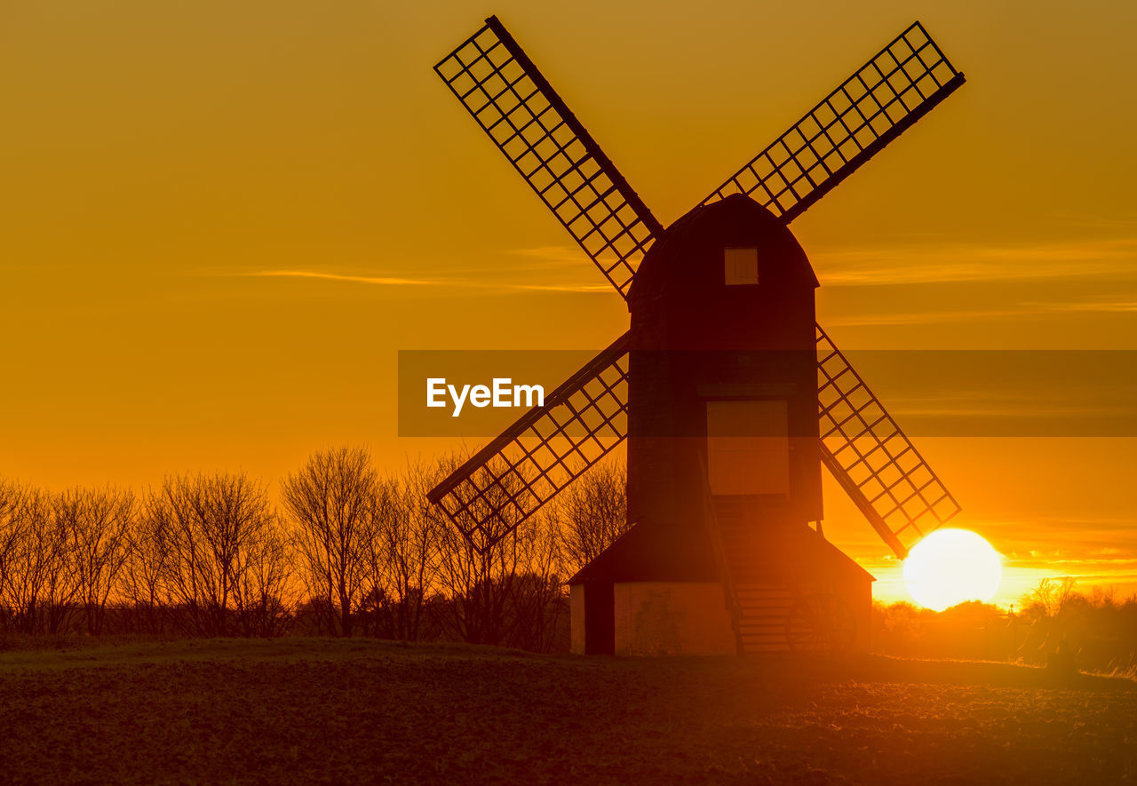 Silhouette of traditional windmill on field against sky during sunset