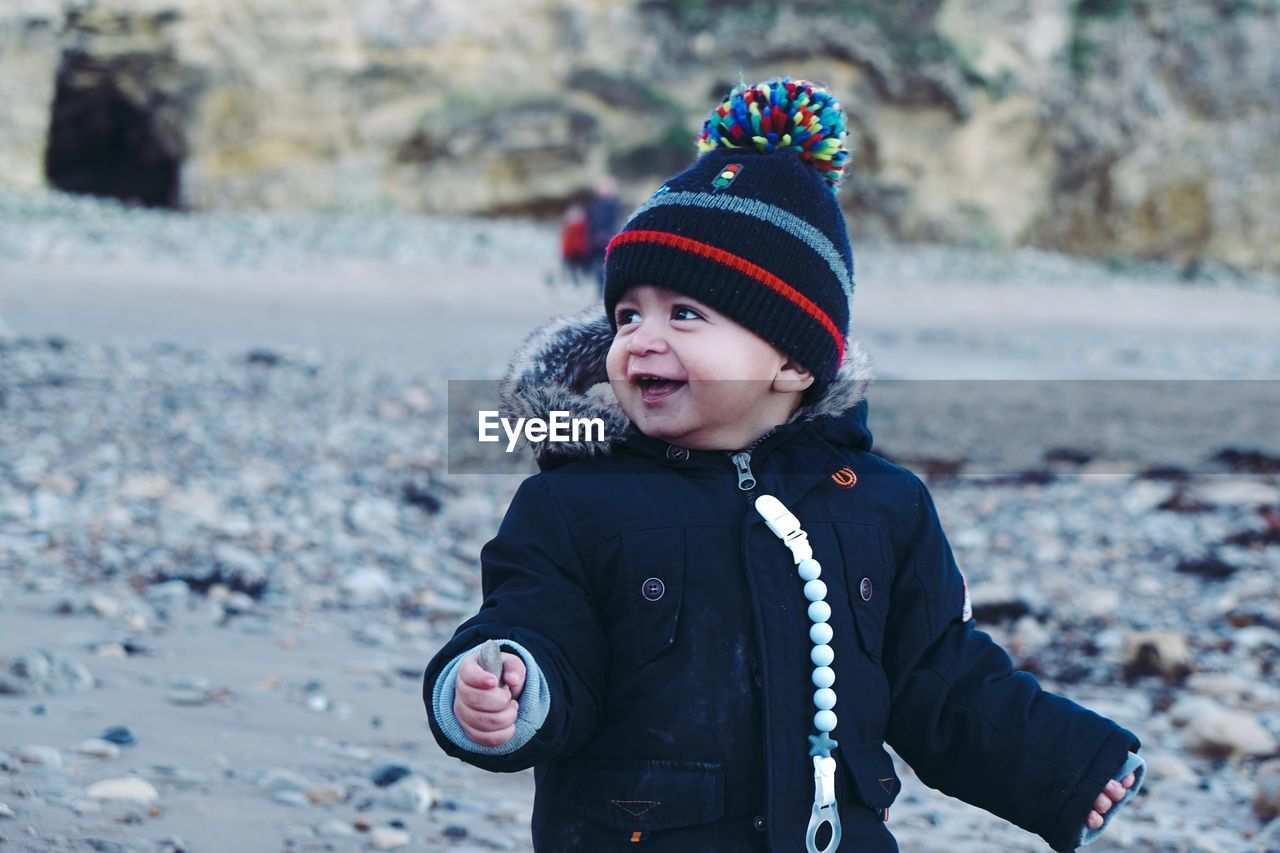 Cute happy baby boy looking away while standing at beach