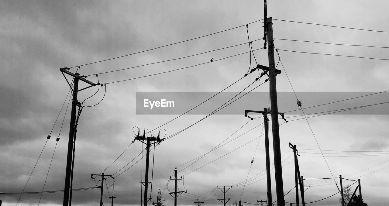 Low angle view of electricity pylon against cloudy sky