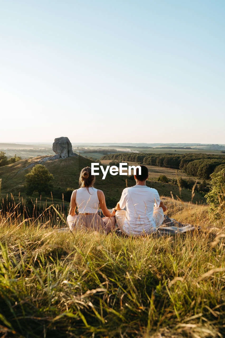 Man and woman practicing yoga and meditation outdoors at sunset with nature miracle giant stone