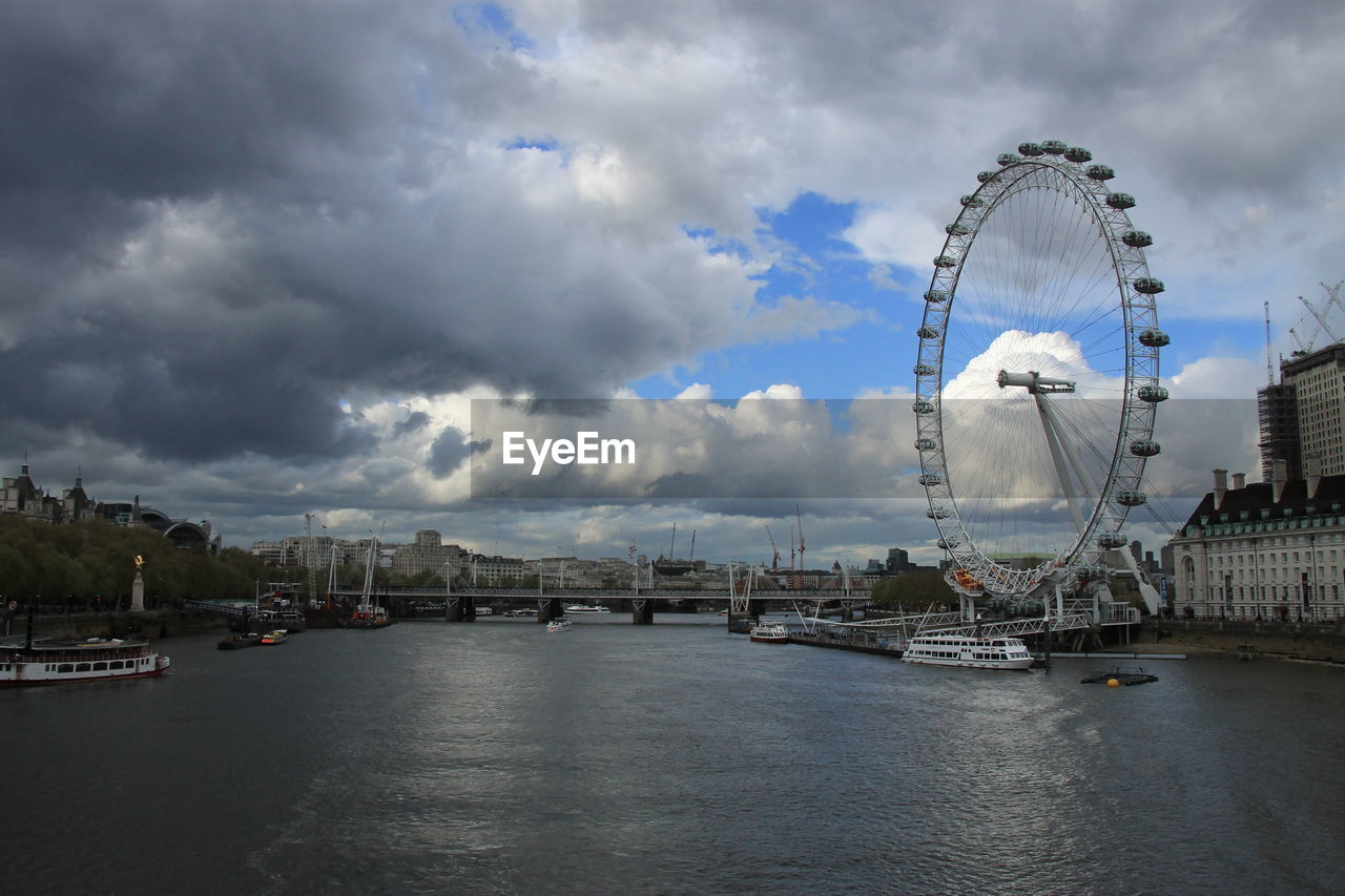 Low angle view of ferris wheel by river in city against sky during sunset