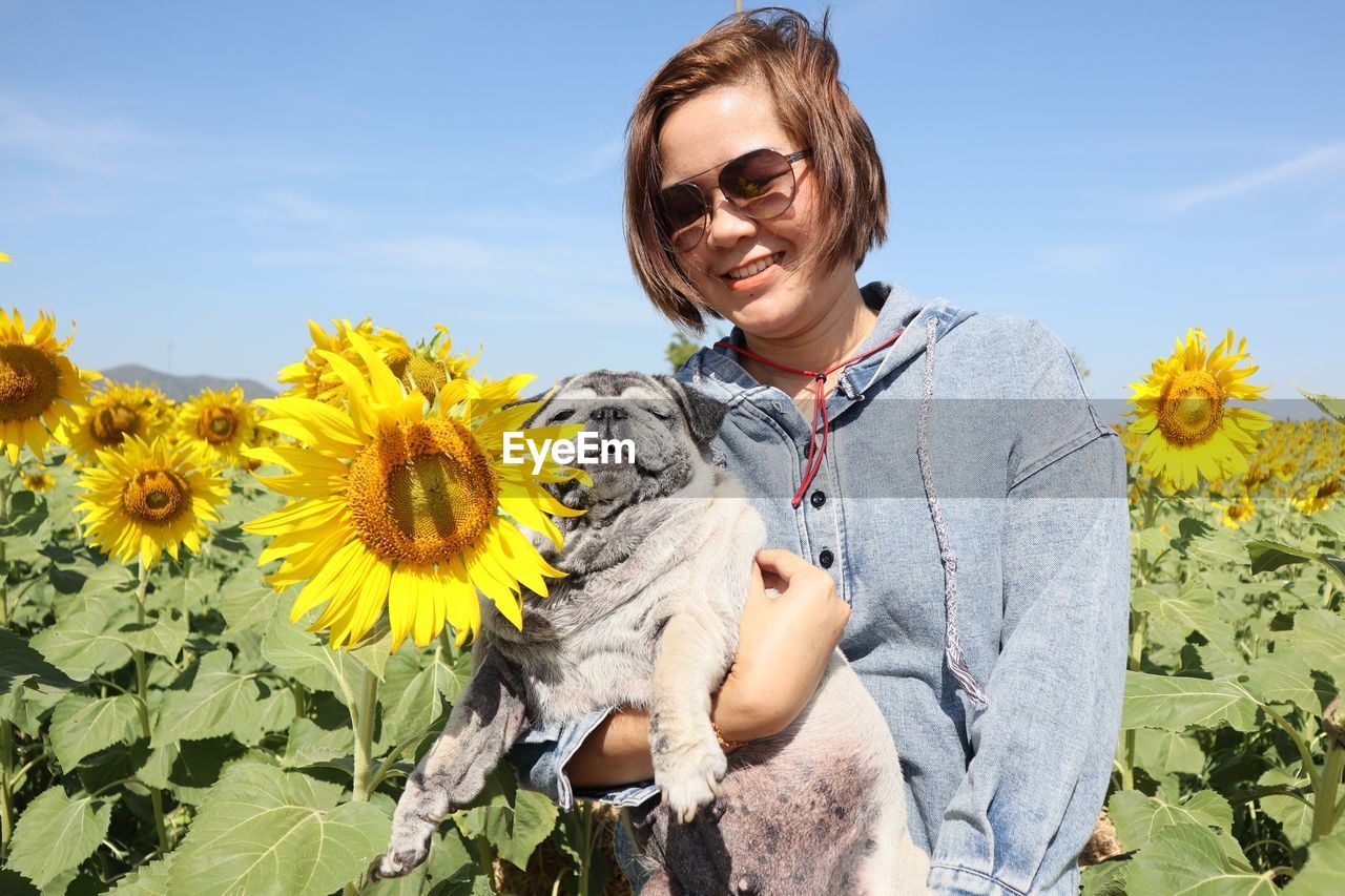 Portrait of smiling woman by sunflower against sky