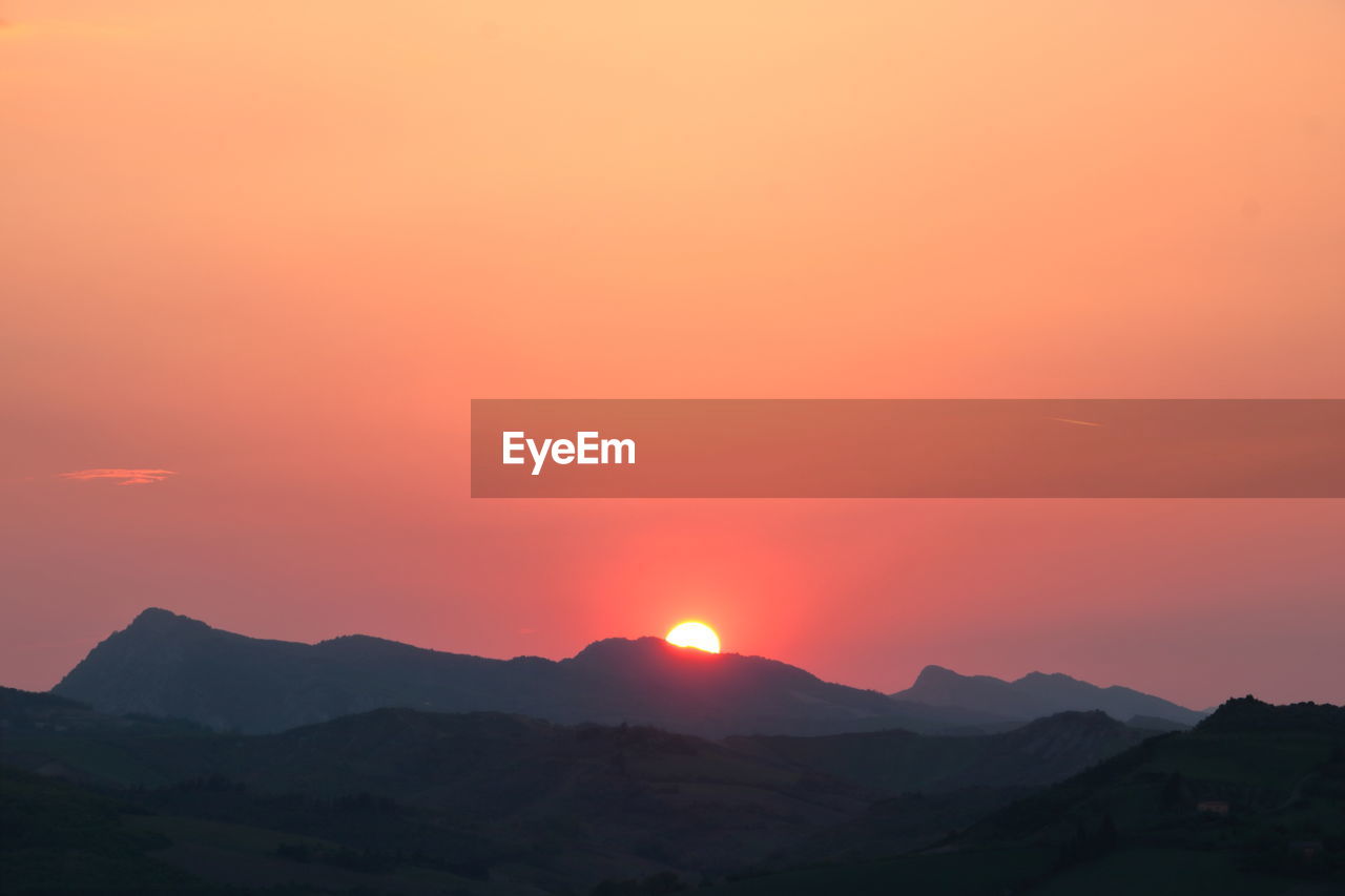 Scenic view of silhouette mountains against orange sky