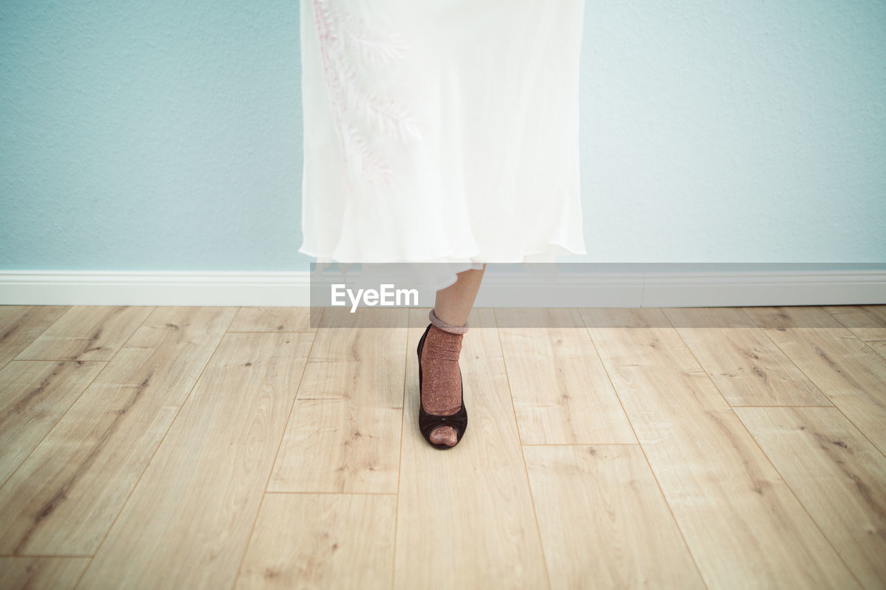 Low section of woman wearing high heels while standing on hardwood floor