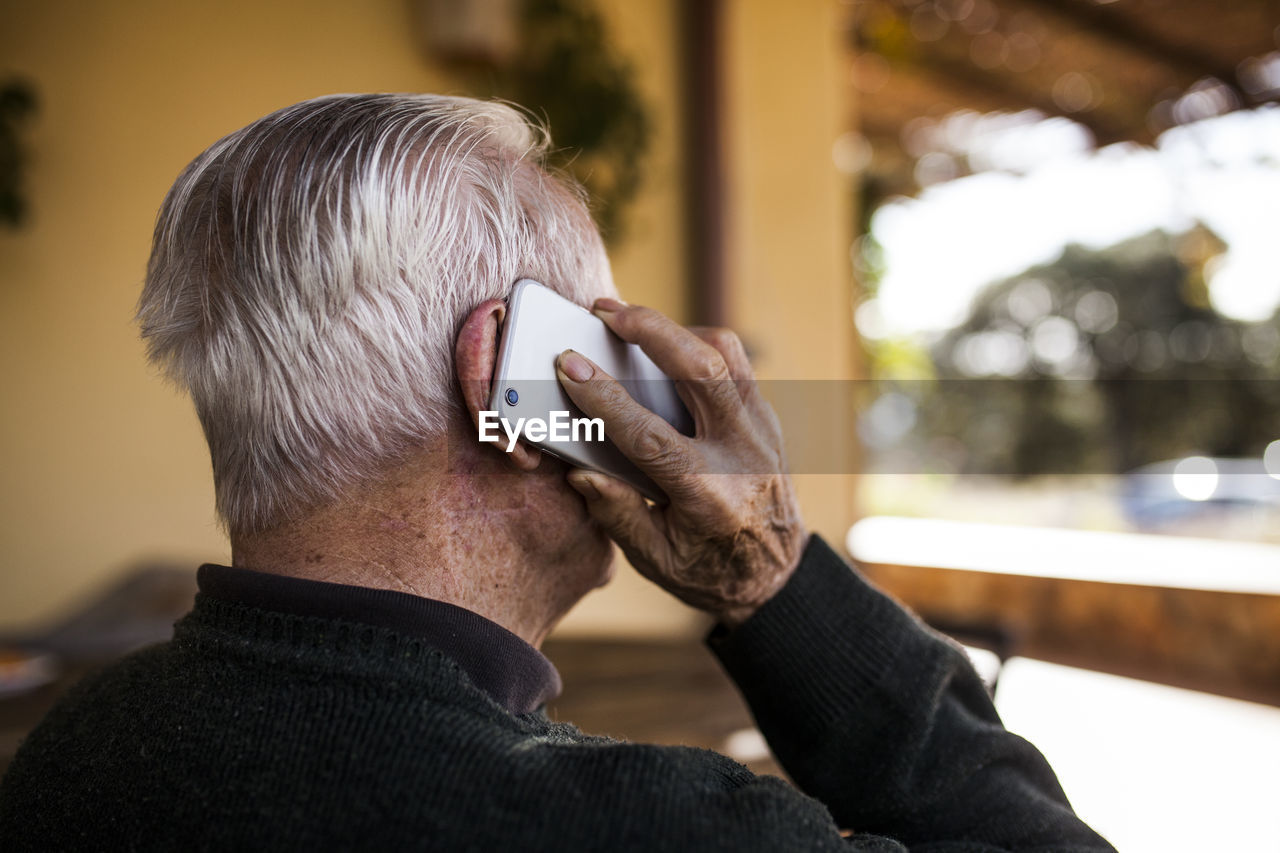 Elderly man talking on the phone on the porch of his house