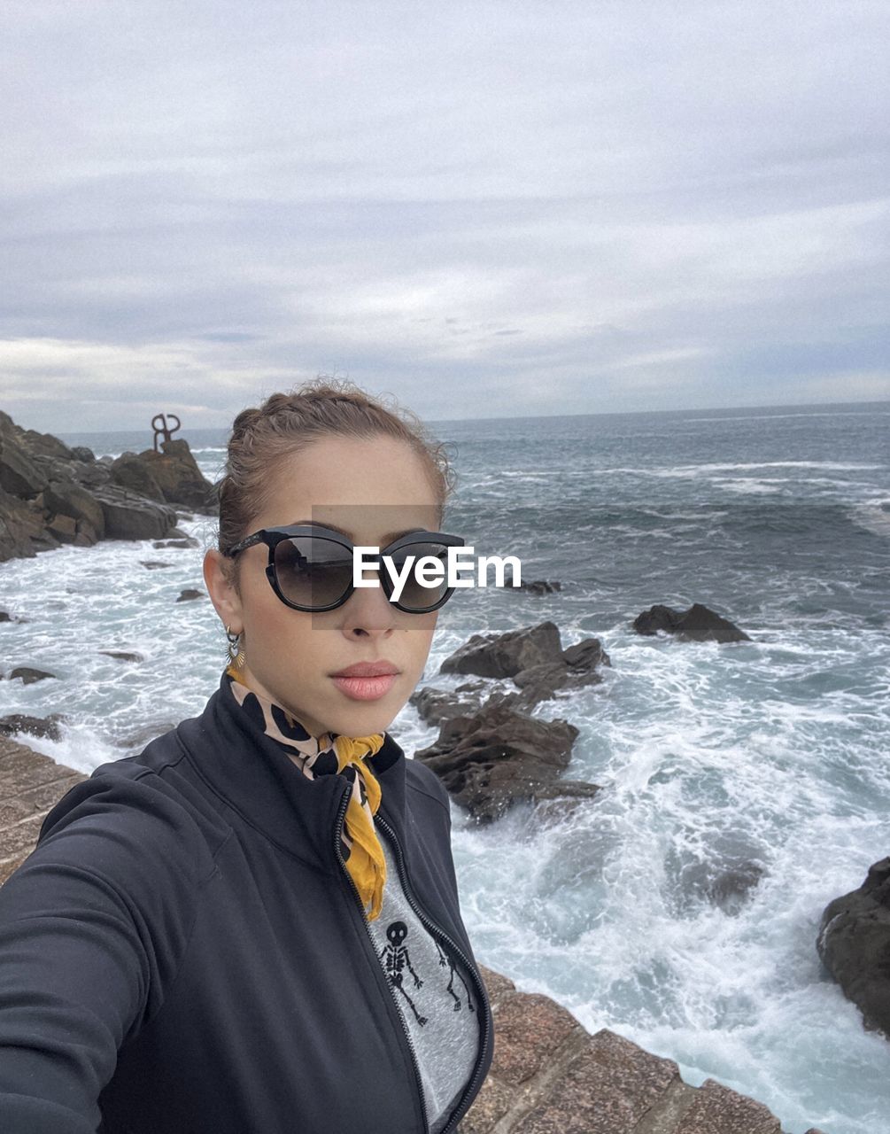 sea, water, glasses, one person, sunglasses, beach, fashion, land, rock, portrait, coast, sky, nature, young adult, leisure activity, adult, beauty in nature, ocean, scenics - nature, cloud, lifestyles, day, outdoors, vacation, trip, holiday, shore, front view, horizon over water, horizon, standing, sports, travel, looking at camera, motion, headshot, waist up, wave, clothing, water sports, travel destinations, tranquility, hairstyle, looking, women