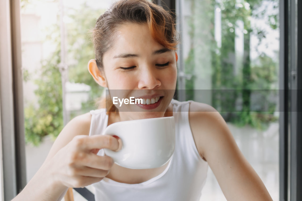 PORTRAIT OF YOUNG WOMAN HOLDING COFFEE CUP