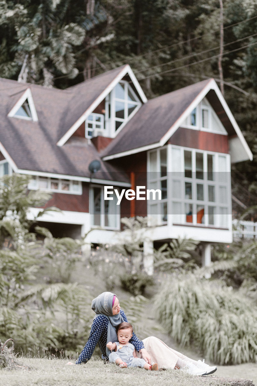 Rear view of girl outside house against trees and building