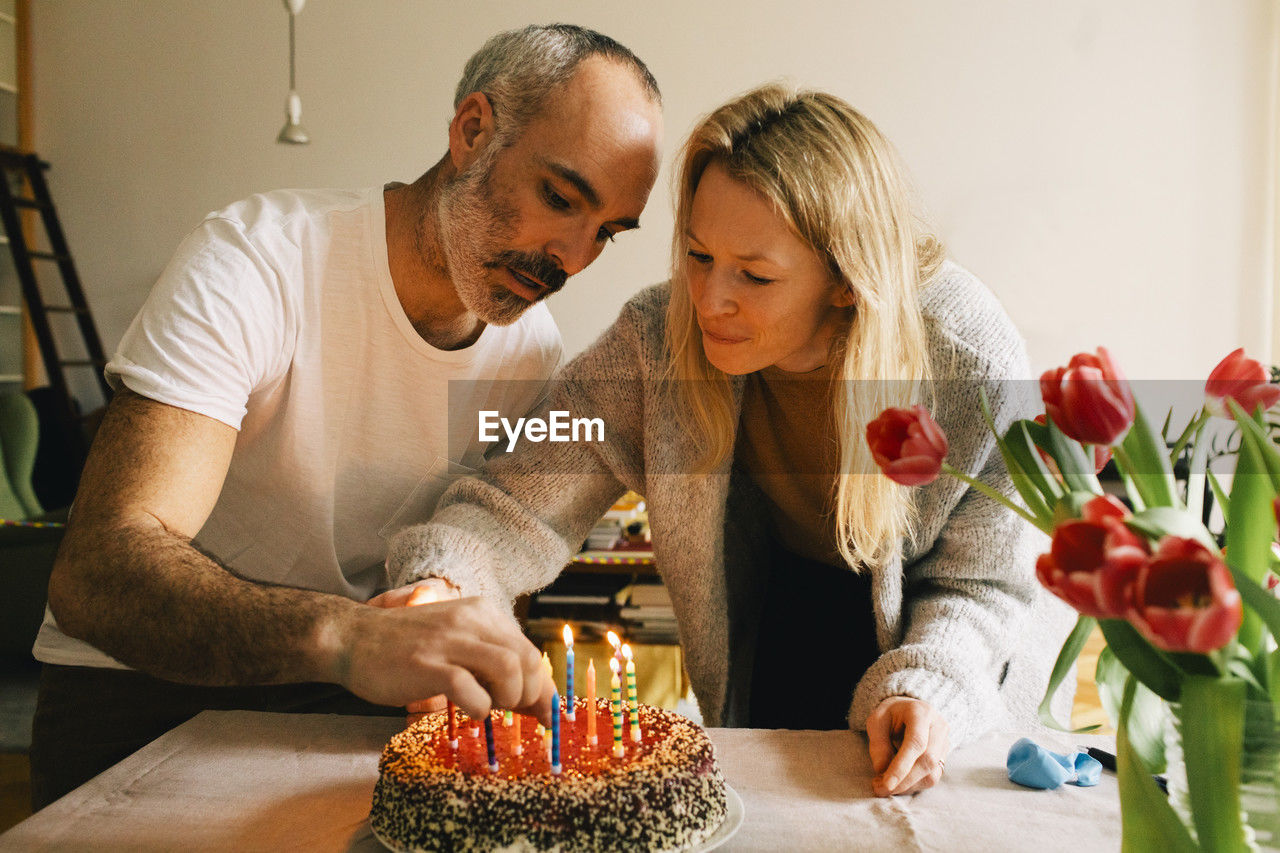 Couple arranging candles on birthday cake together at home