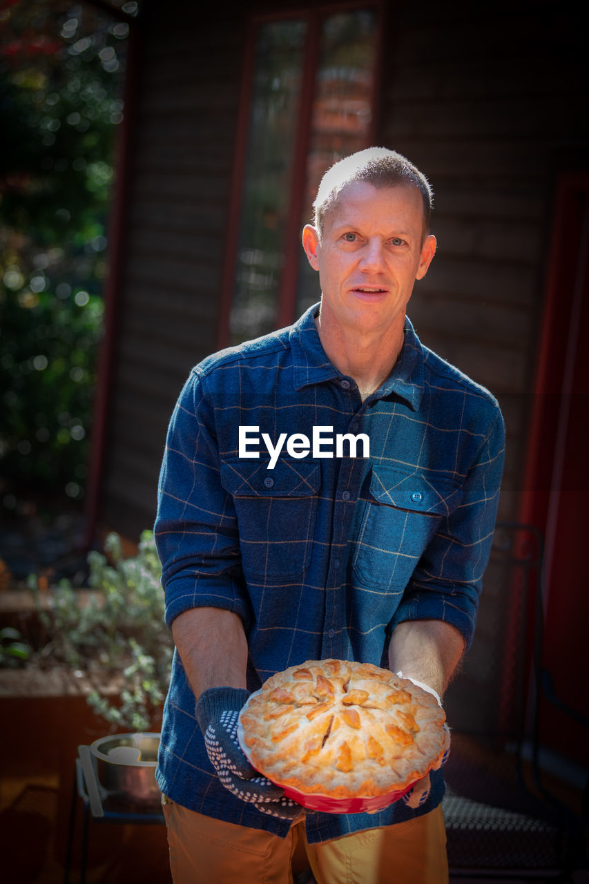 Portrait of mature man holding sweet pie outside house