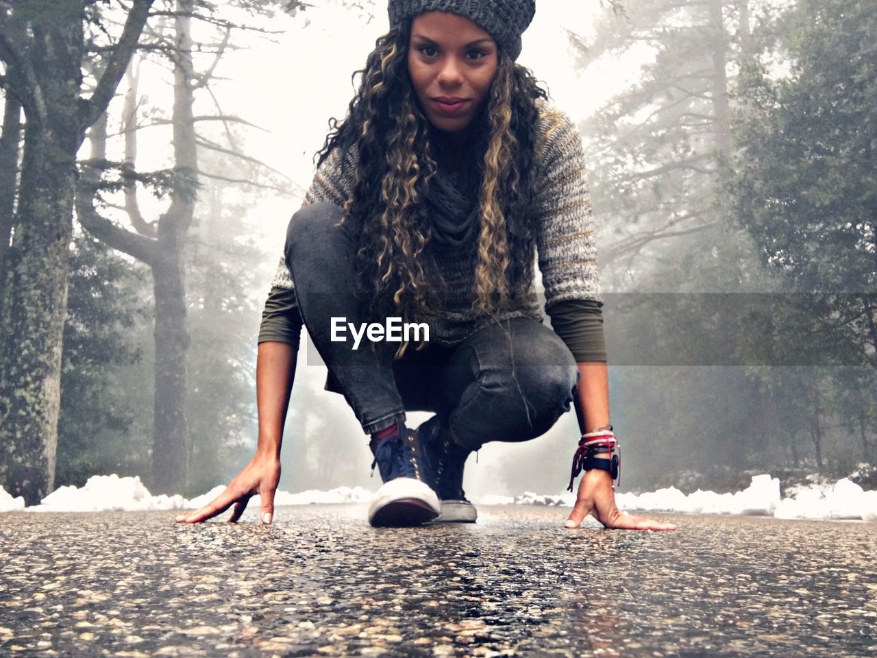 Portrait of beautiful woman crouching on street amidst trees during winter