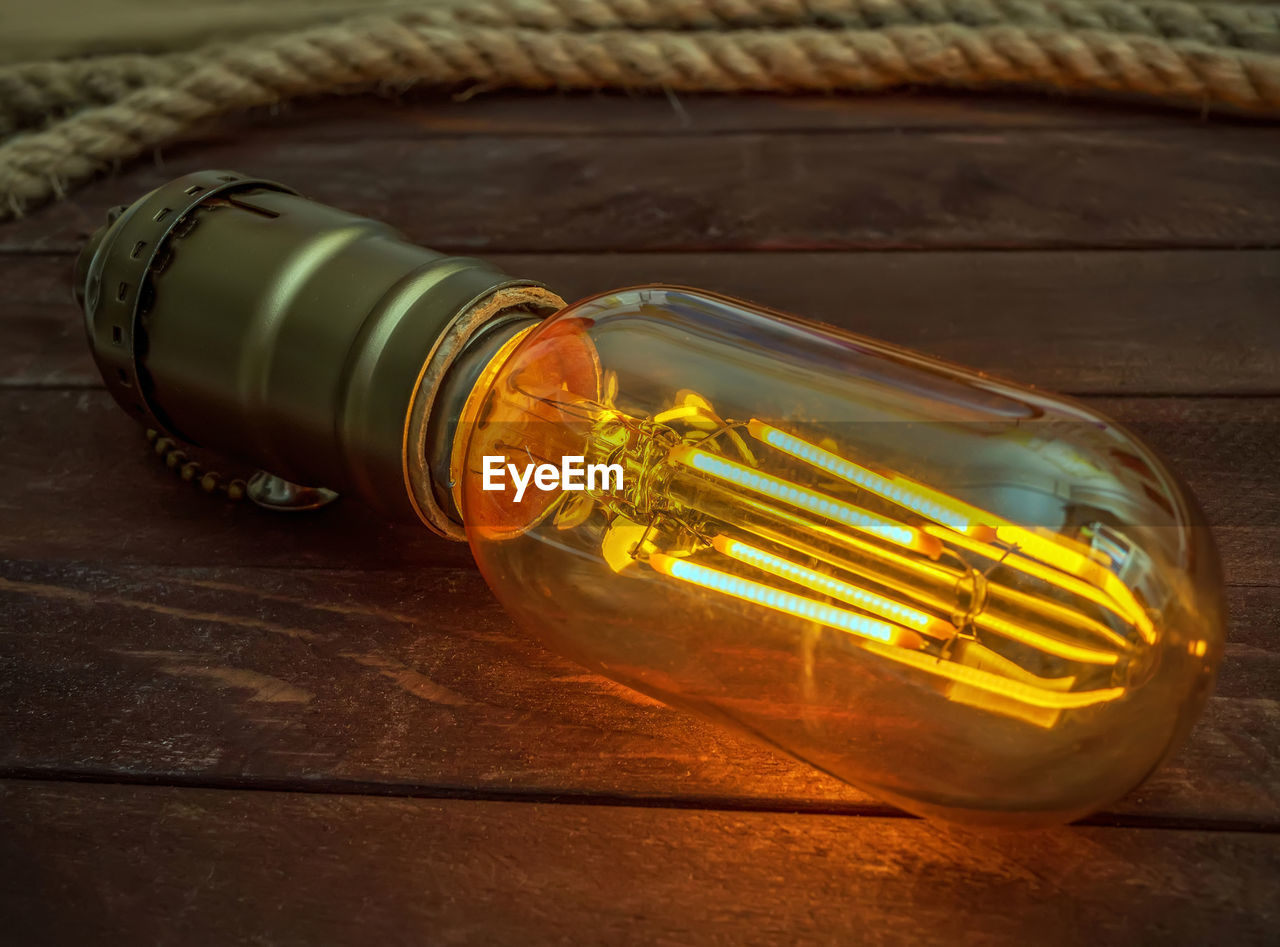 Led filament light bulb with an amber-colored glass shell on the background of dark brown boards. 