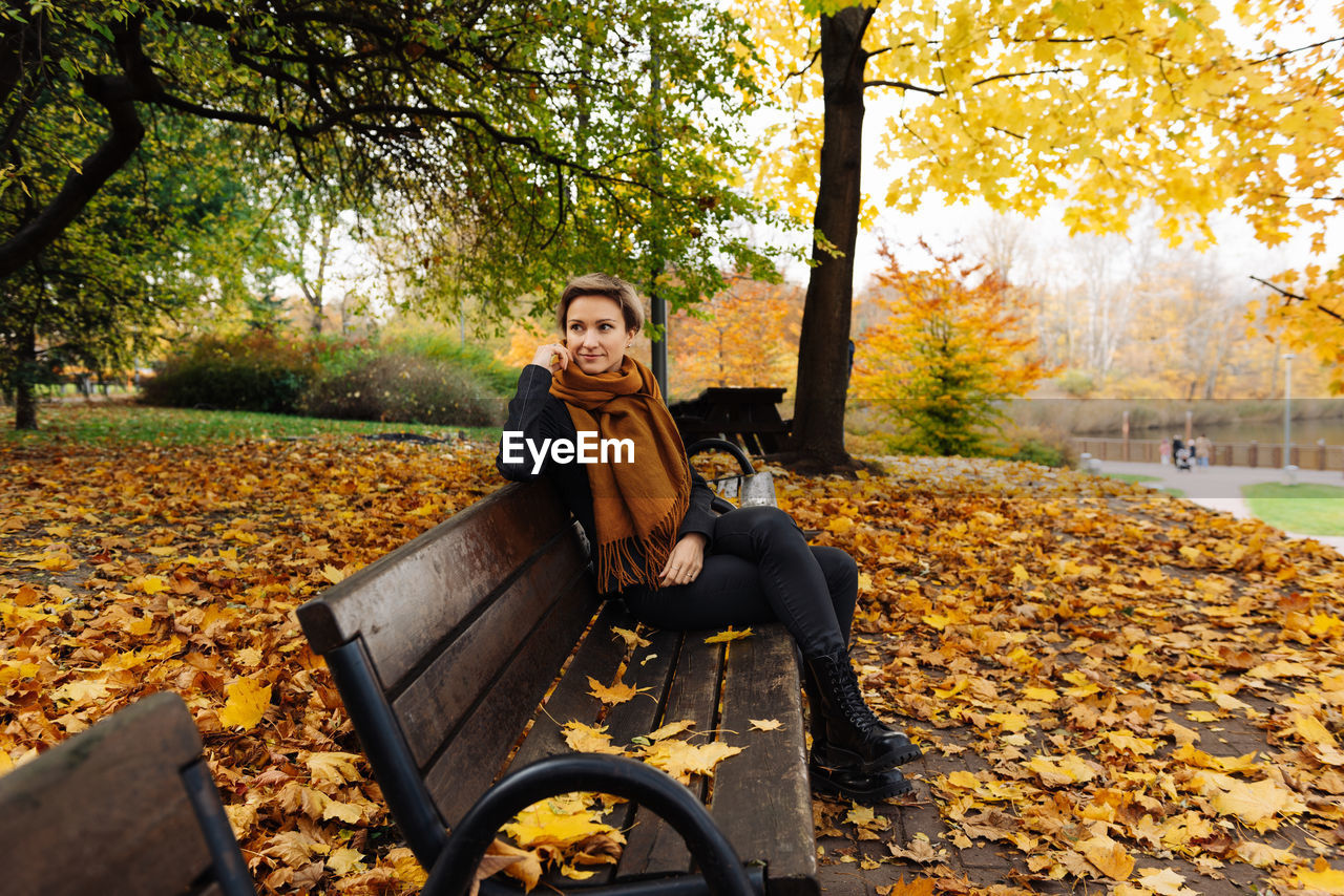 Short-haired blonde rests in an autumn park sitting on a bench