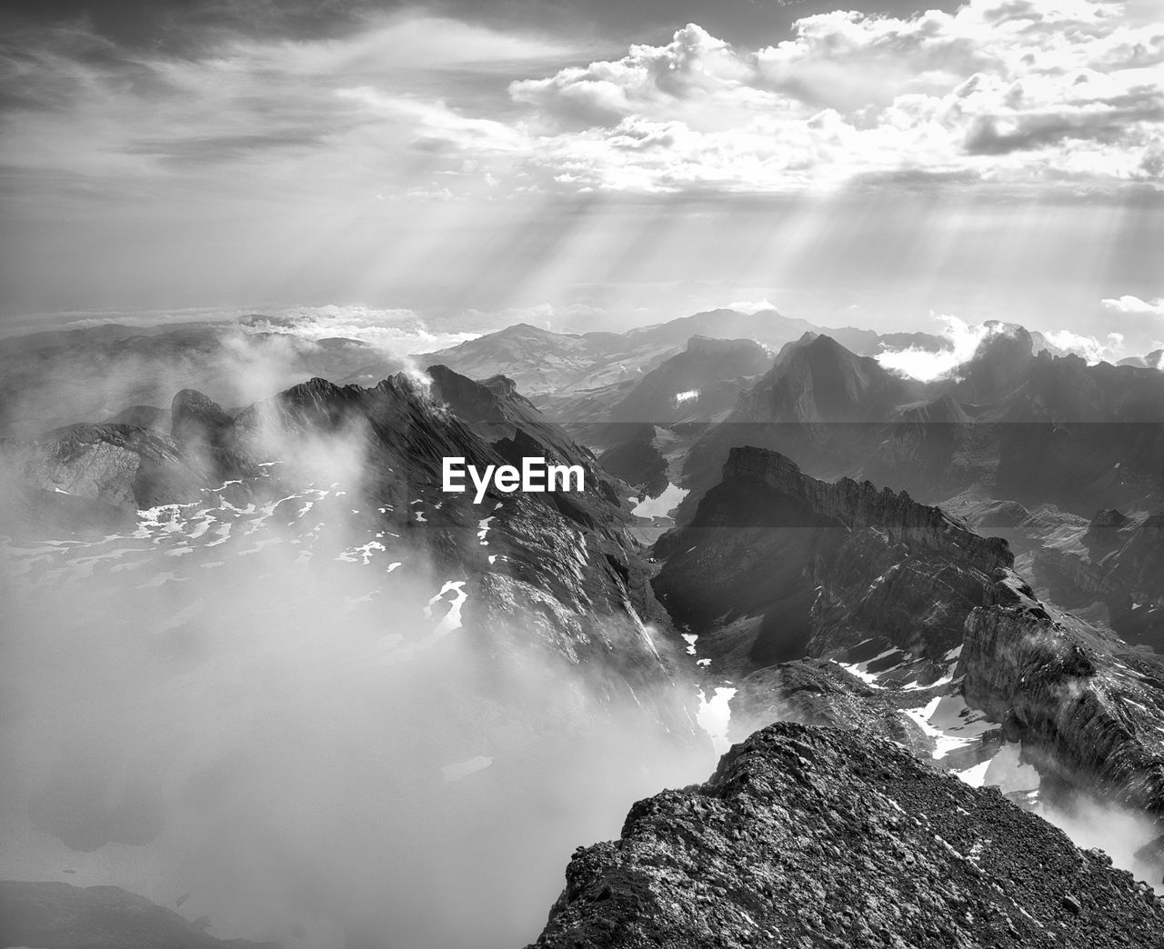 mountain, environment, scenics - nature, black and white, cloud, landscape, beauty in nature, sky, monochrome, monochrome photography, mountain range, nature, fog, land, travel, mountain peak, cold temperature, travel destinations, rock, snow, outdoors, cloudscape, no people, tranquility, winter, white, water, high up, tourism, sunbeam, tranquil scene, non-urban scene, dramatic sky, sunlight, awe, darkness, horizon, idyllic, snowcapped mountain, sun