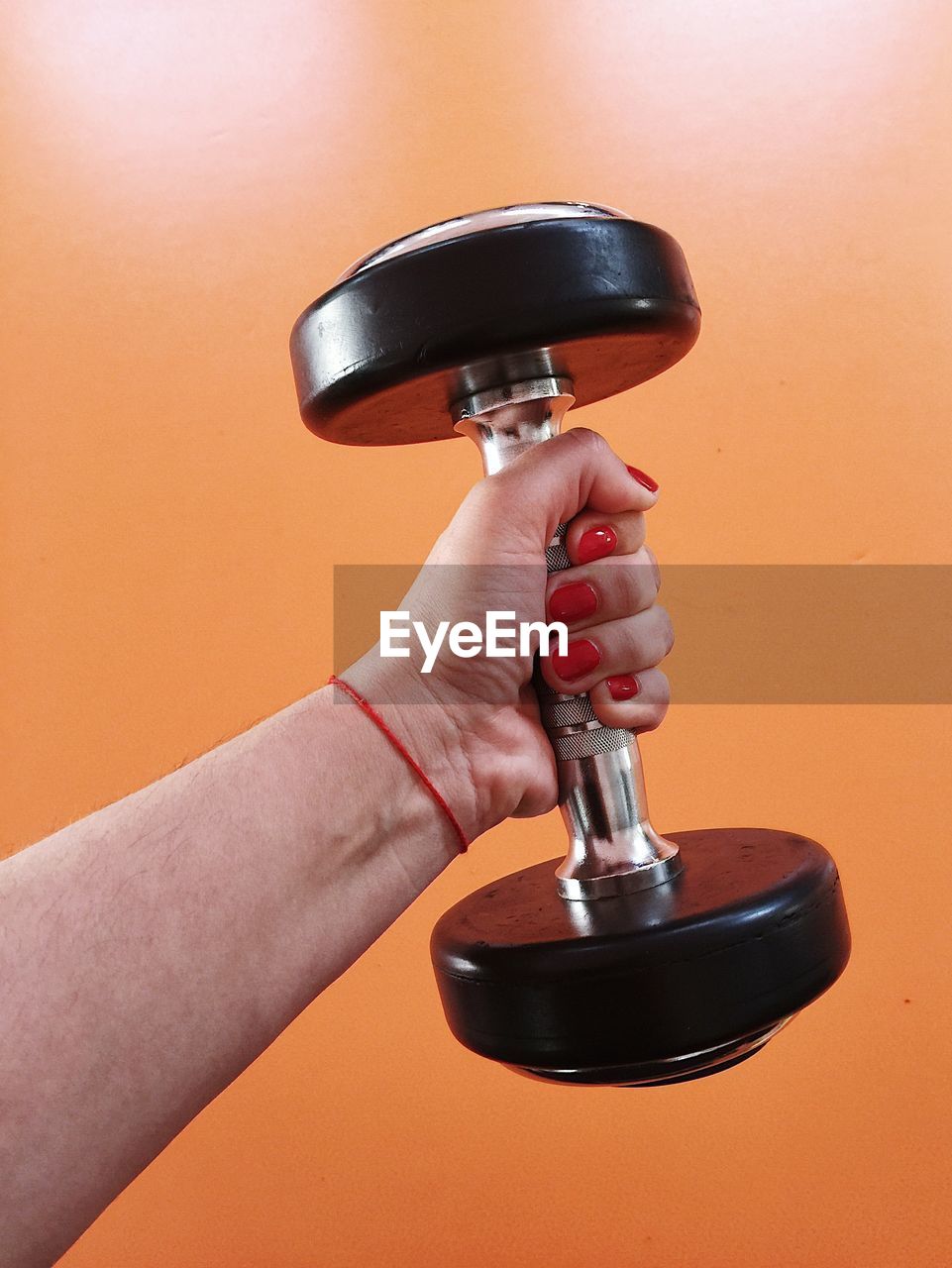 Close-up of woman holding dumbbell against orange background