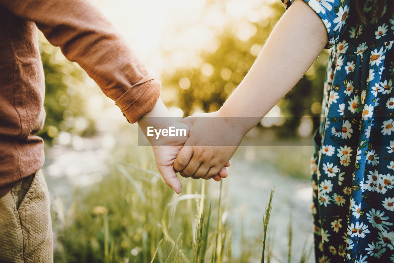 Midsection of siblings holding hands on field