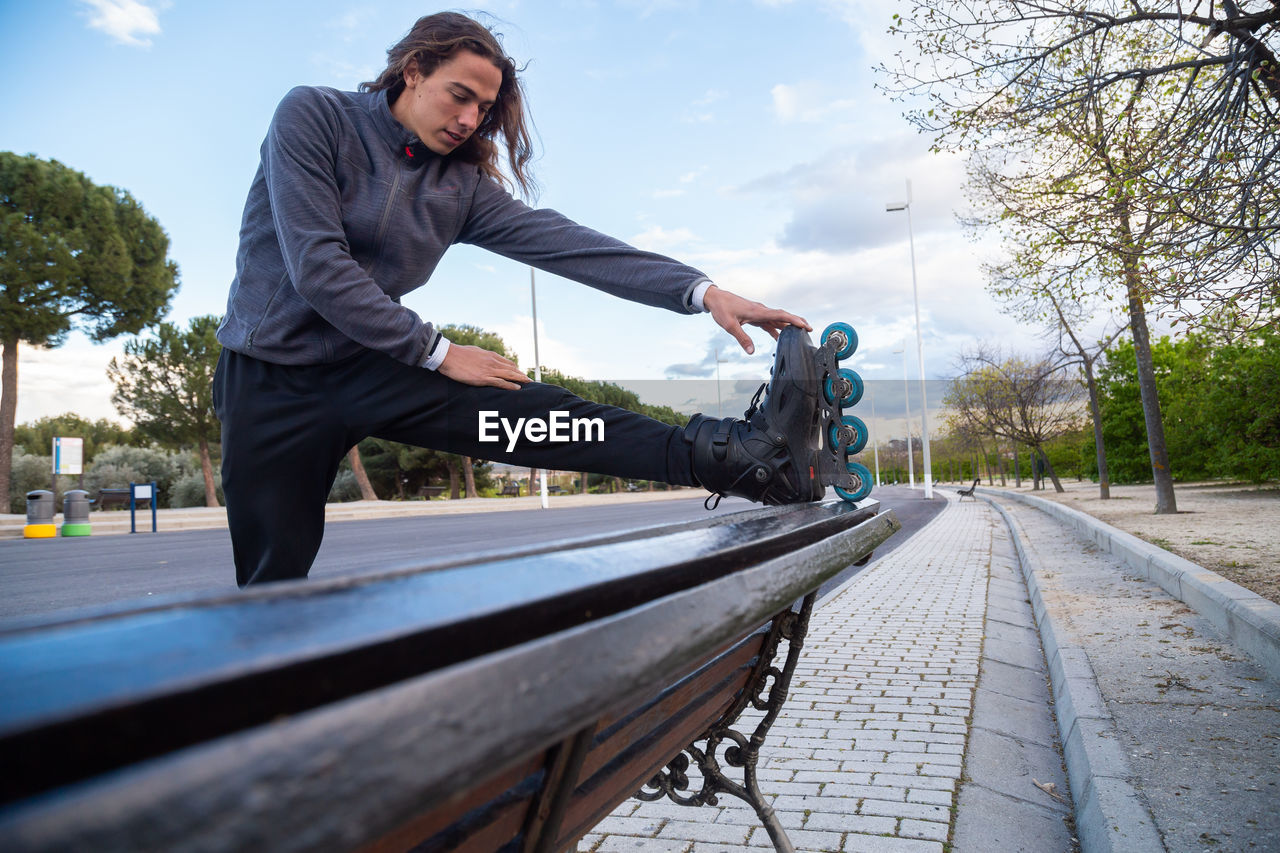 Young man wearing roller skates stretching on bench