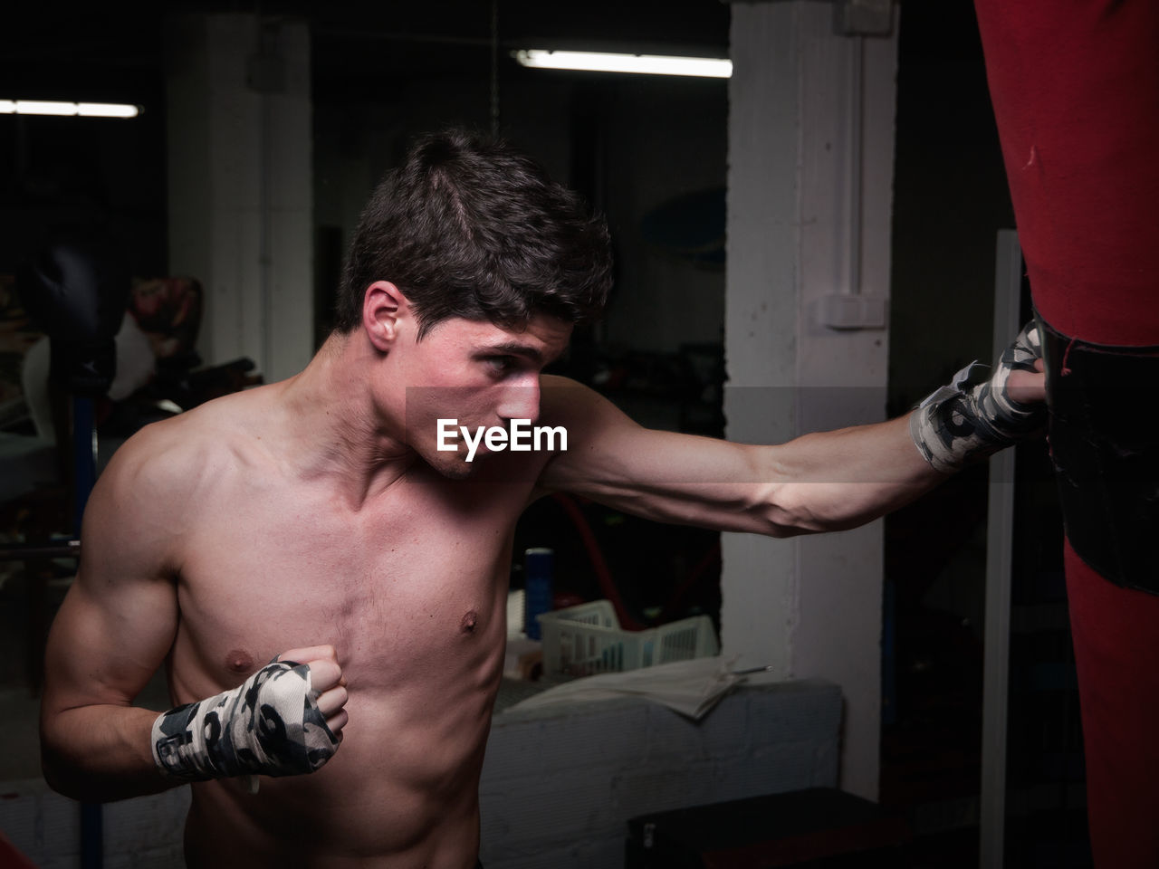 Shirtless man punching bag in boxing rink