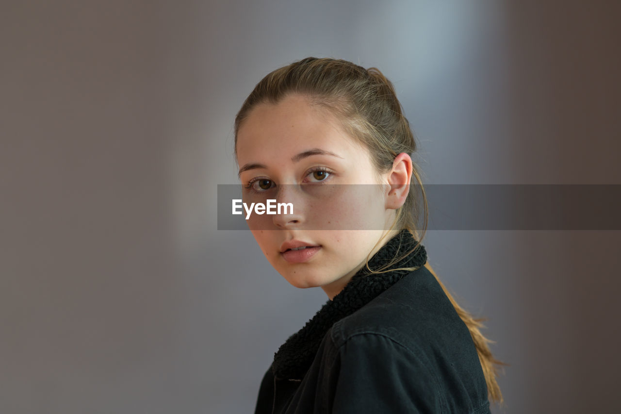 Pretty teenage girl with ponytail hair posing looking at the camera over a grey background