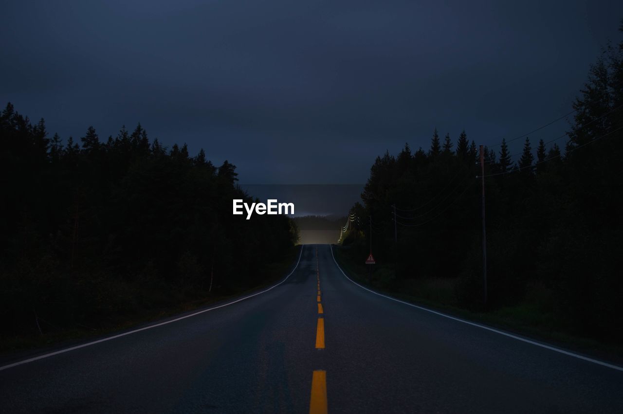 Empty road along trees at night