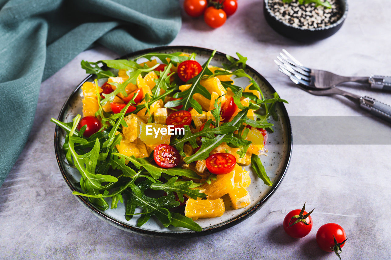 Dietary salad of orange slices, cherry tomatoes and arugula on a plate on the table