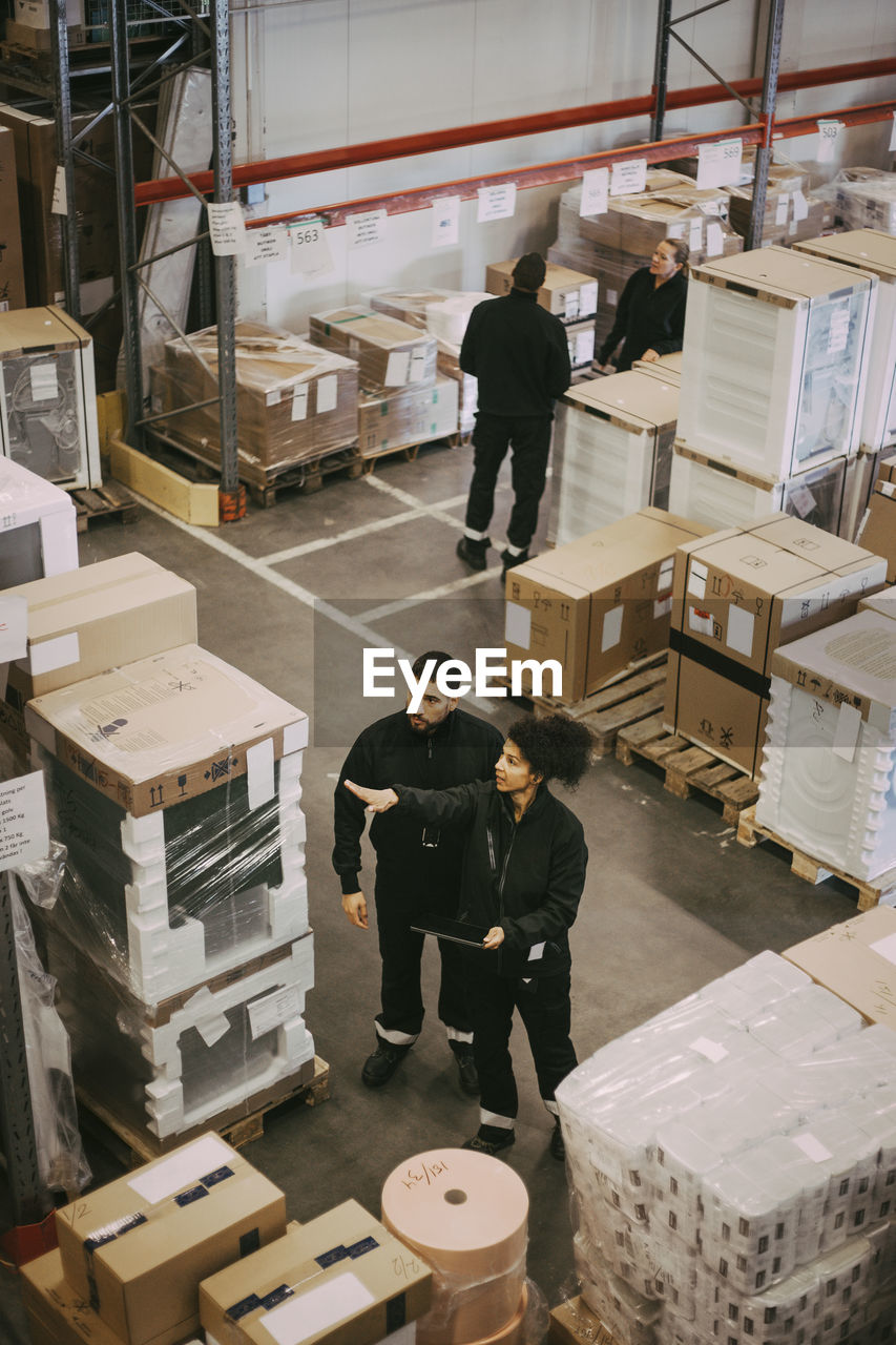 High angle view of male and female manual worker analyzing at distribution warehouse