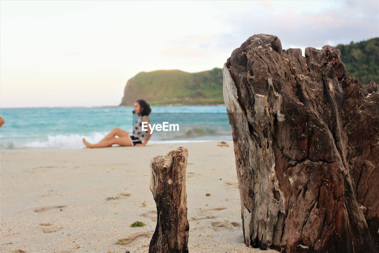 Woman sitting on beach against sky