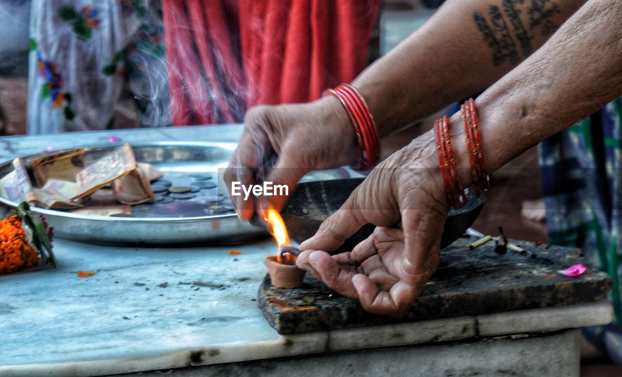 Cropped hands of women igniting diya in temple