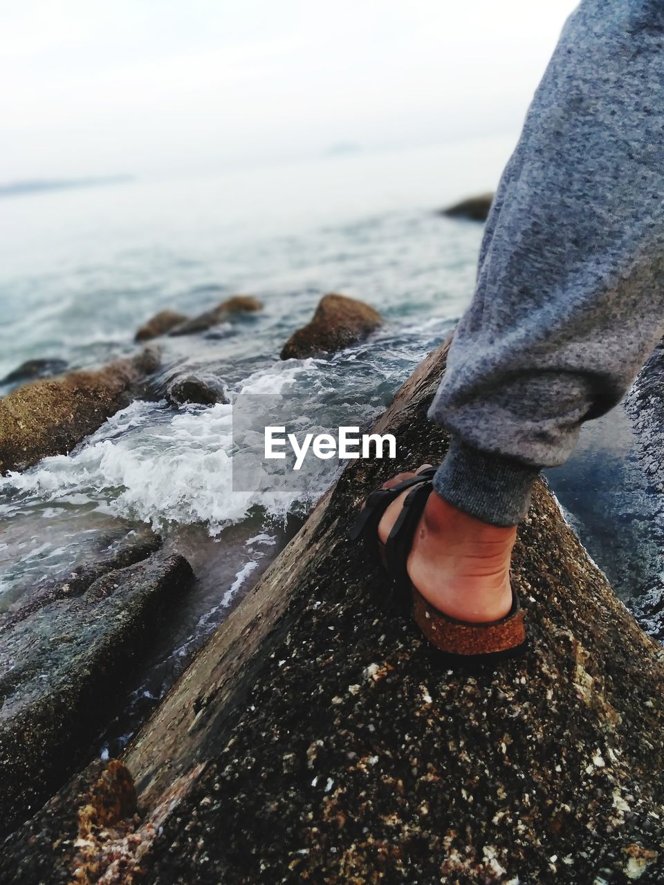 Low section of man standing on rock at beach