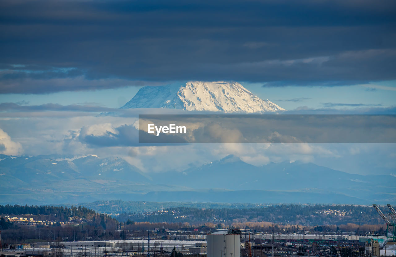 Clouds partially cover mount rainier which towers over the port of tacoma.