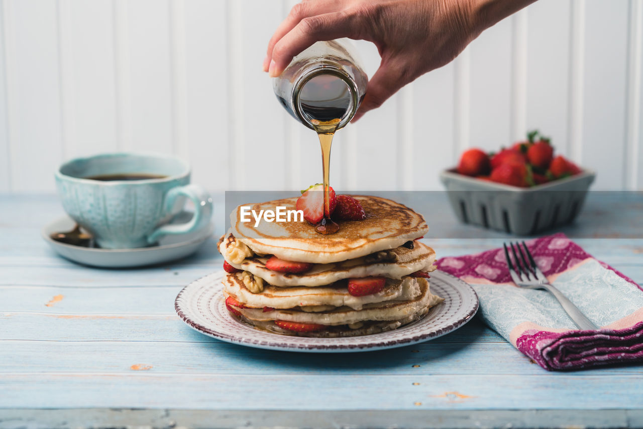Close-up of person pouring honey on pancake 